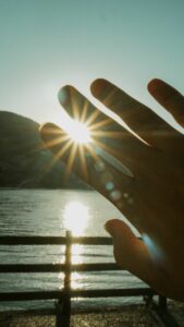 A hand silhouette capturing sunrays and reflections by a serene lake, evoking tranquility.